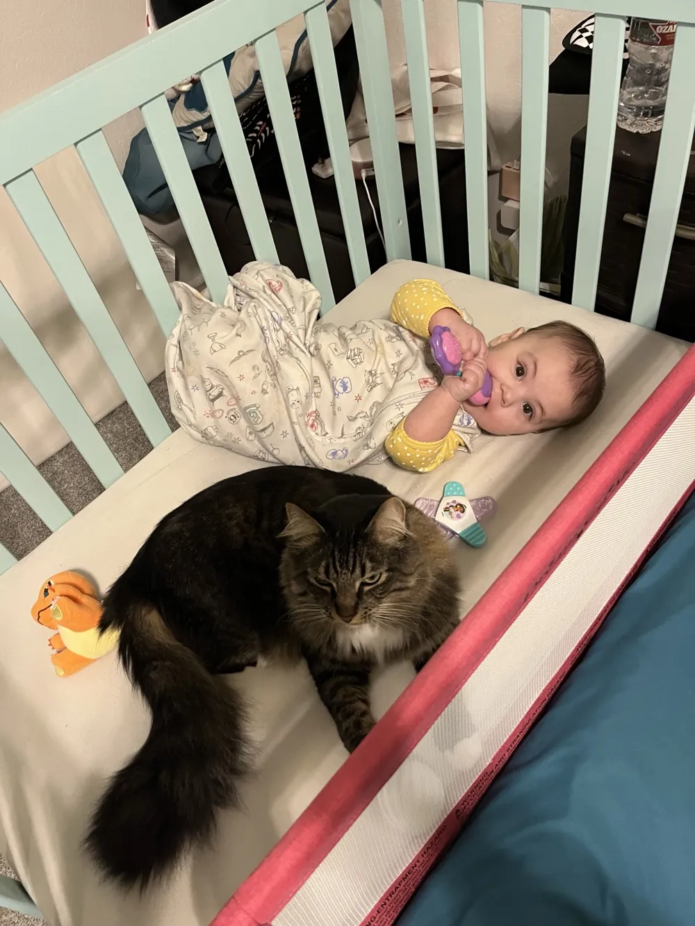 Oliver Mittens lying in a crib beside a baby